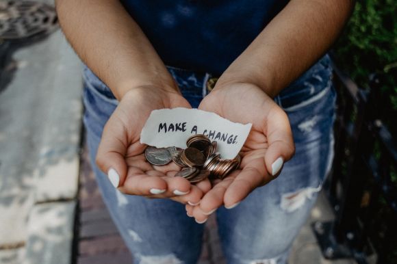Charity - person showing both hands with make a change note and coins