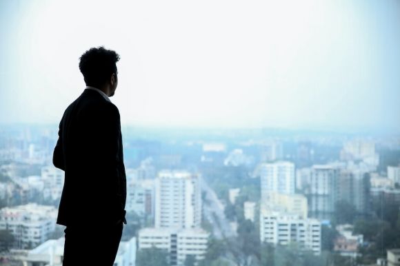 Businessman - man in black suit standing on top of building looking at city buildings during daytime