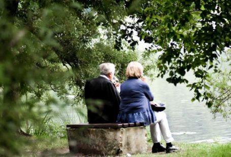 Elderly Couple - two people sitting on pavement facing on body of water