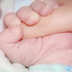 Parental Security - Touching moment of crop anonymous newborn infant with tiny hand lying on soft bed and gently grasping parents finger
